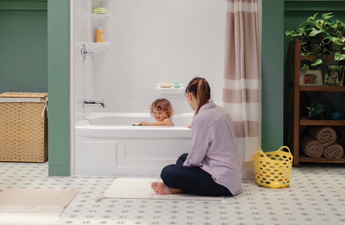 A mom is seated in front of the bathtub while her daughter plays with a toy car.