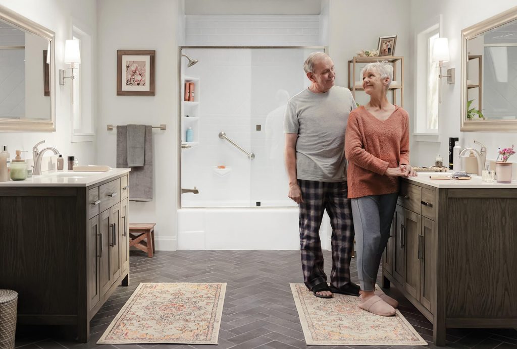 An older couple exchanges a smile at the sink with their newly renovated bathtub glistening behind them.