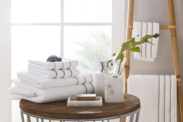 Bathroom towels folded on a round wooden table and others hanging from bamboo storage ladder