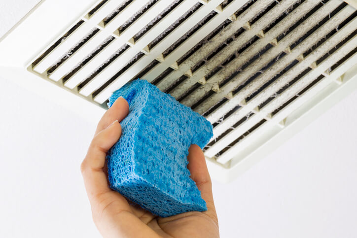 A hand with scourer cleaning a dirty ceiling vent