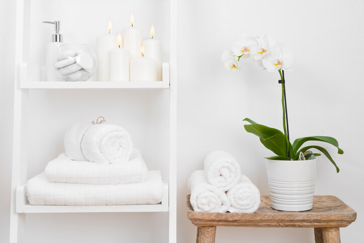 An orchid in a white pot with rolled up towels next to it on a stool