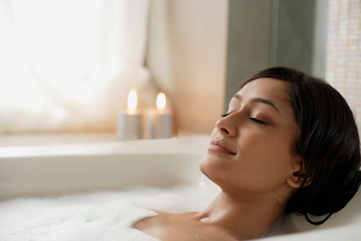 Woman relaxing in a foamy bathtub with candles