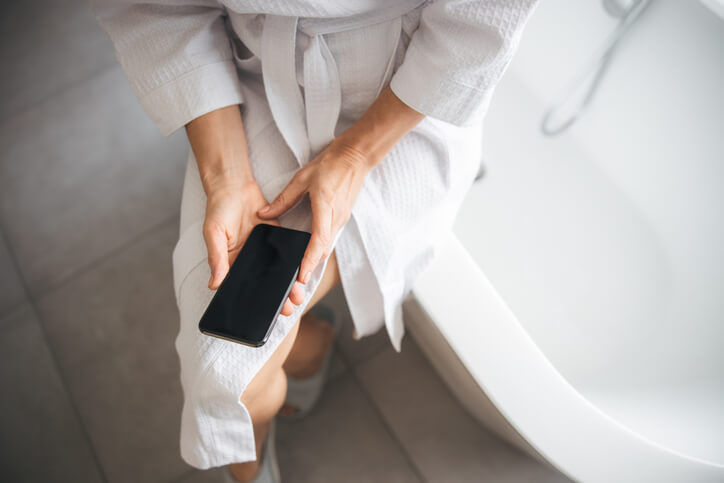 Woman sitting on the edge of a bathtub and holding her smartphone