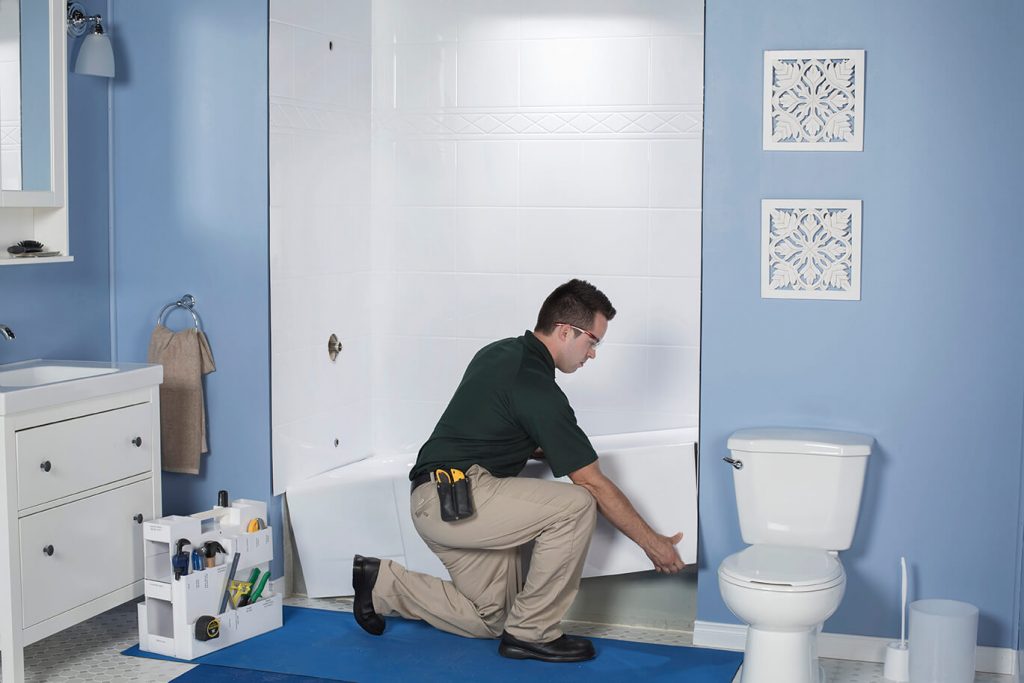 A Bath Fitter installer kneels on the floor while installing a new bathtub over an old one