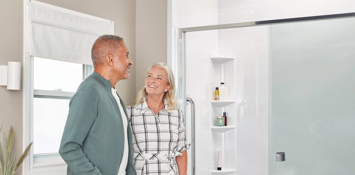 A man and woman stand in their renovated bathroom gazing happily at their new shower