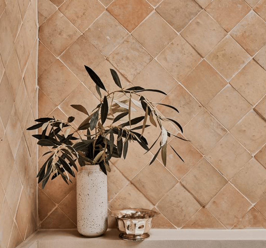 A stone vase with a plant sits on the edge of a tub with a backdrop of terracotta tiles