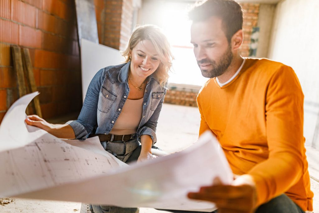 a man and a woman sit on the floor holding plans of what seems to be their remodeled bathroom