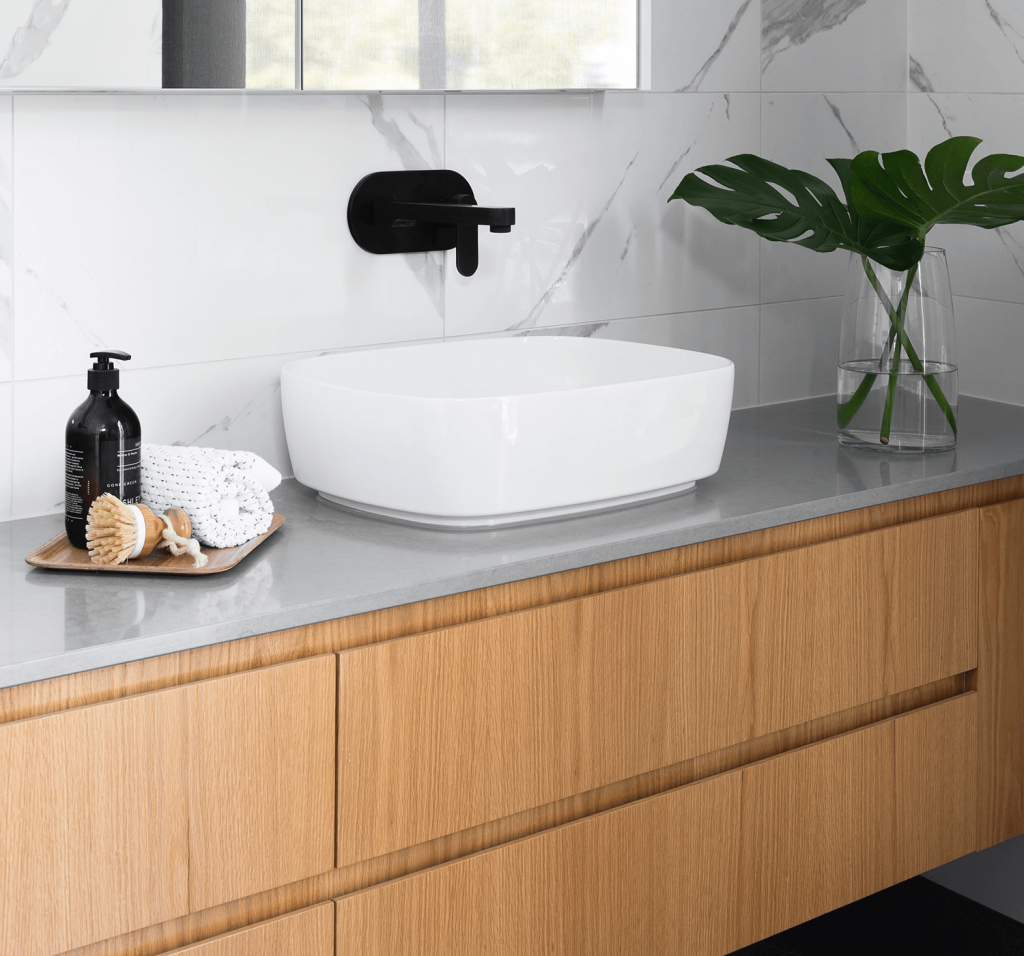 A wooden floating vanity is against a white tiled wall with a circular white sink