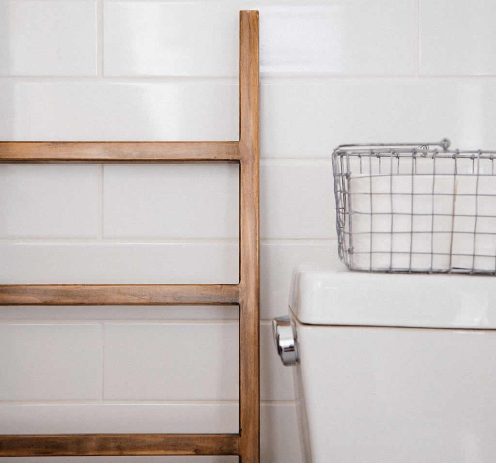 A wooden ladder stands up against a white tiled wall beside a toilet