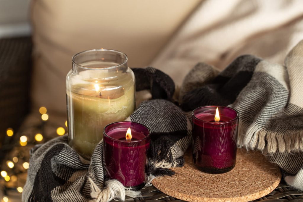 three lit decorative candles lit and surrounded by a black and white plaid blanket