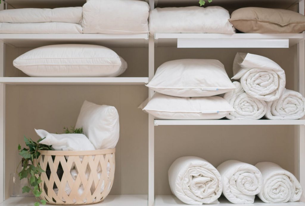 an open shelf with rolled white towels and pillows neatly placed