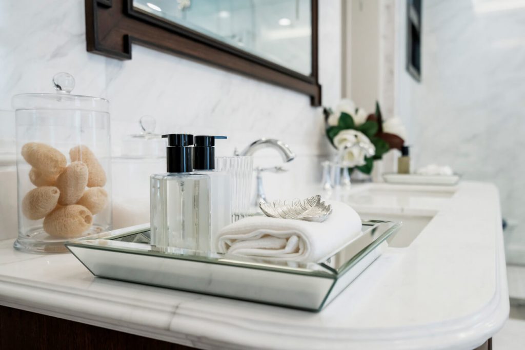 a mirrored tray holding a hand towel and products sits on a marble topped vanity