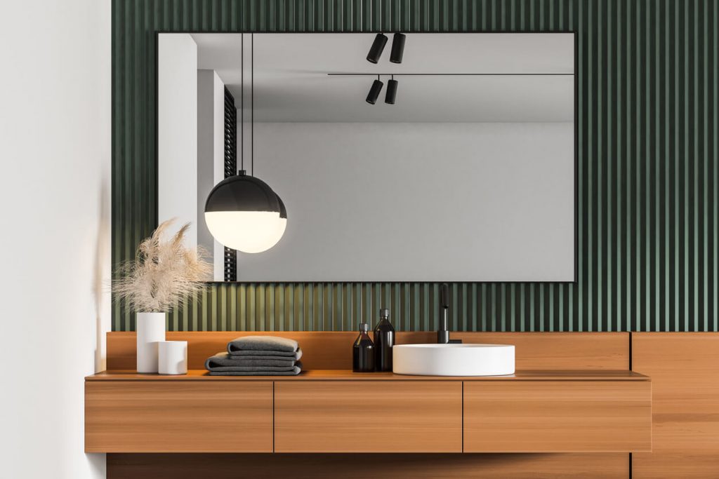 a modern bathroom with floating wooden vanity holding towels and vases against a green textured wall