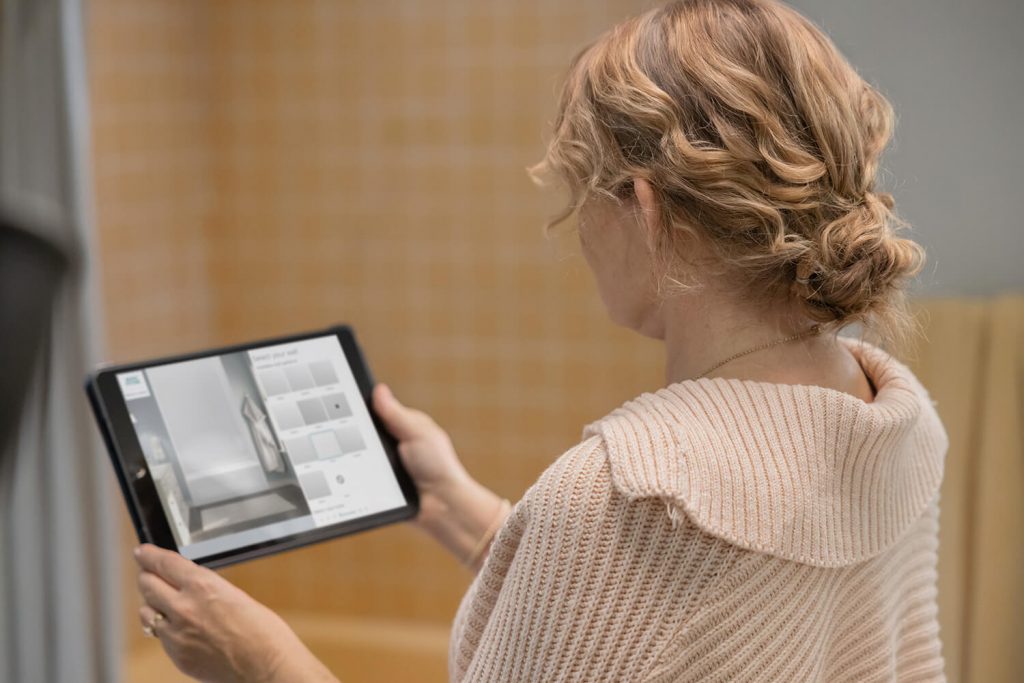 A woman stands before her unrenovated bathtub while playing around with new bathroom designs on her iPad.