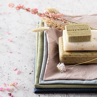 Three bars of soap sit on top of cotton towels on a stone surface