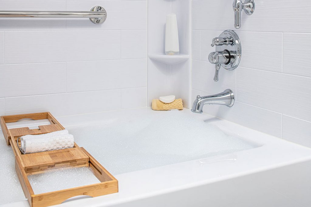 A wooden tray is shown resting on a white bathtub filled with bubbles