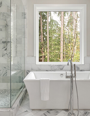 A square white cast polymer bathtub is free-standing next to a shower