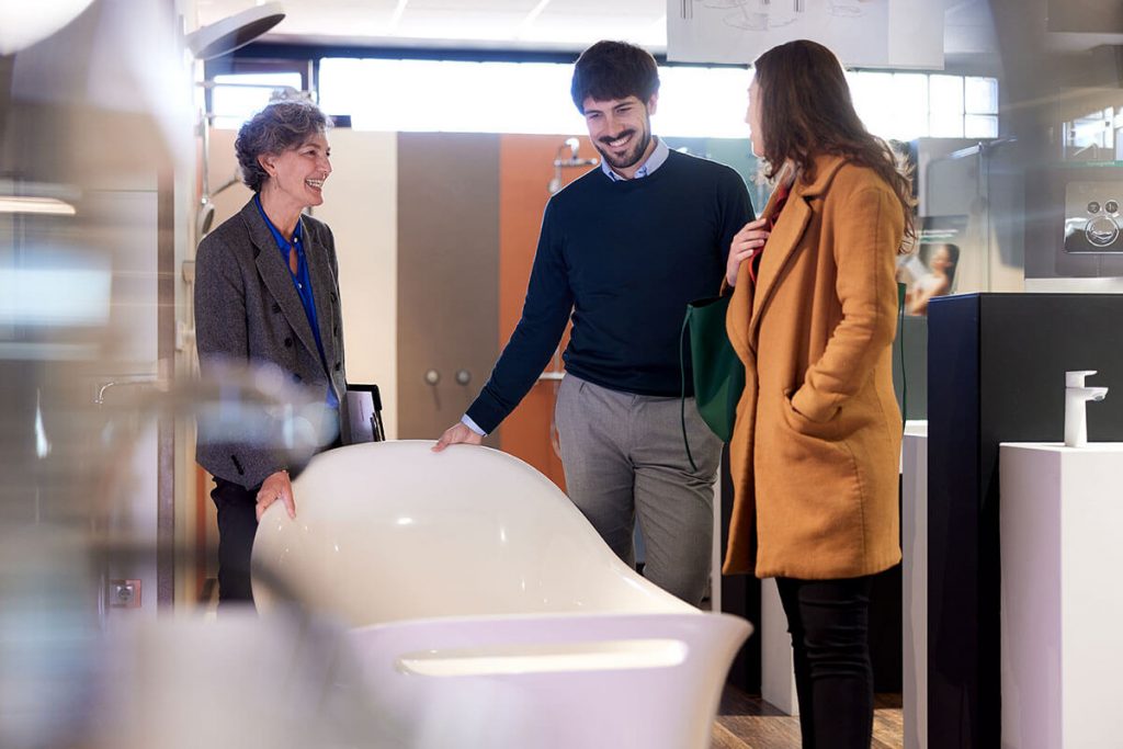 A couple is shown a bathtub by a store clerk in a warehouse