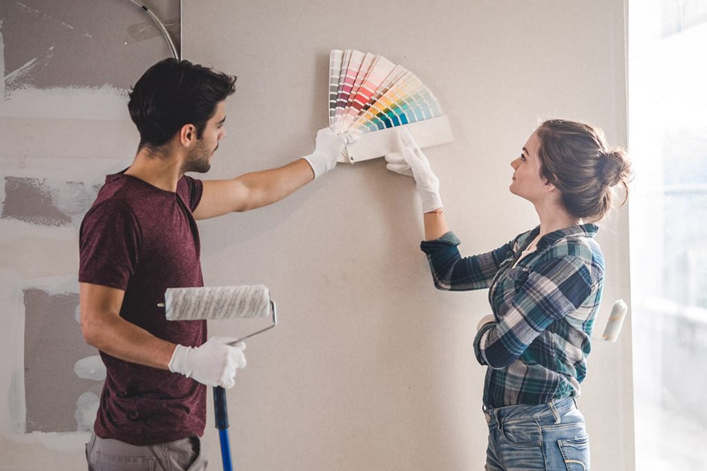 A couple choosing color swatches for painting against a wall