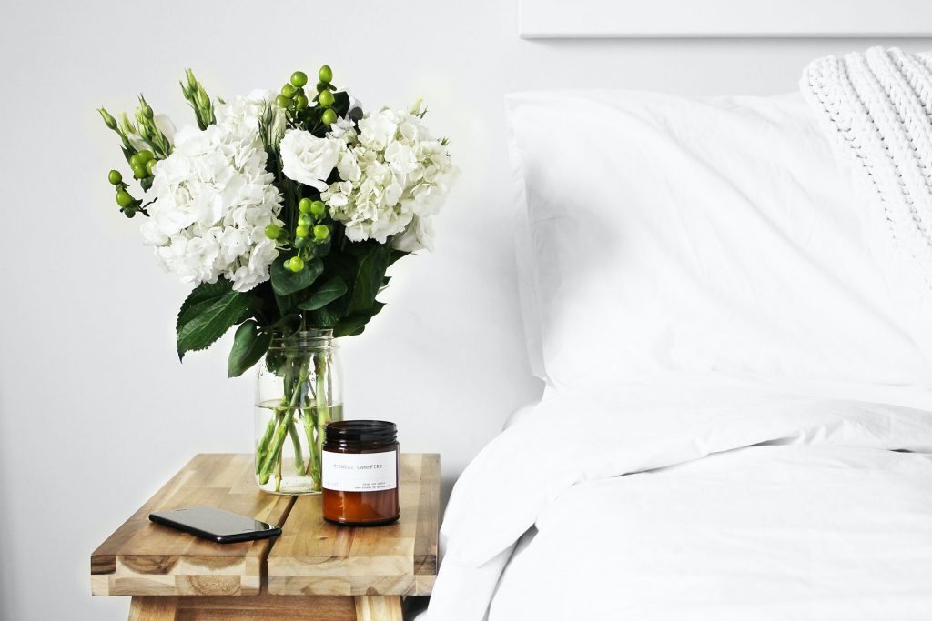 White bed beside fresh flowers on a nightstand
