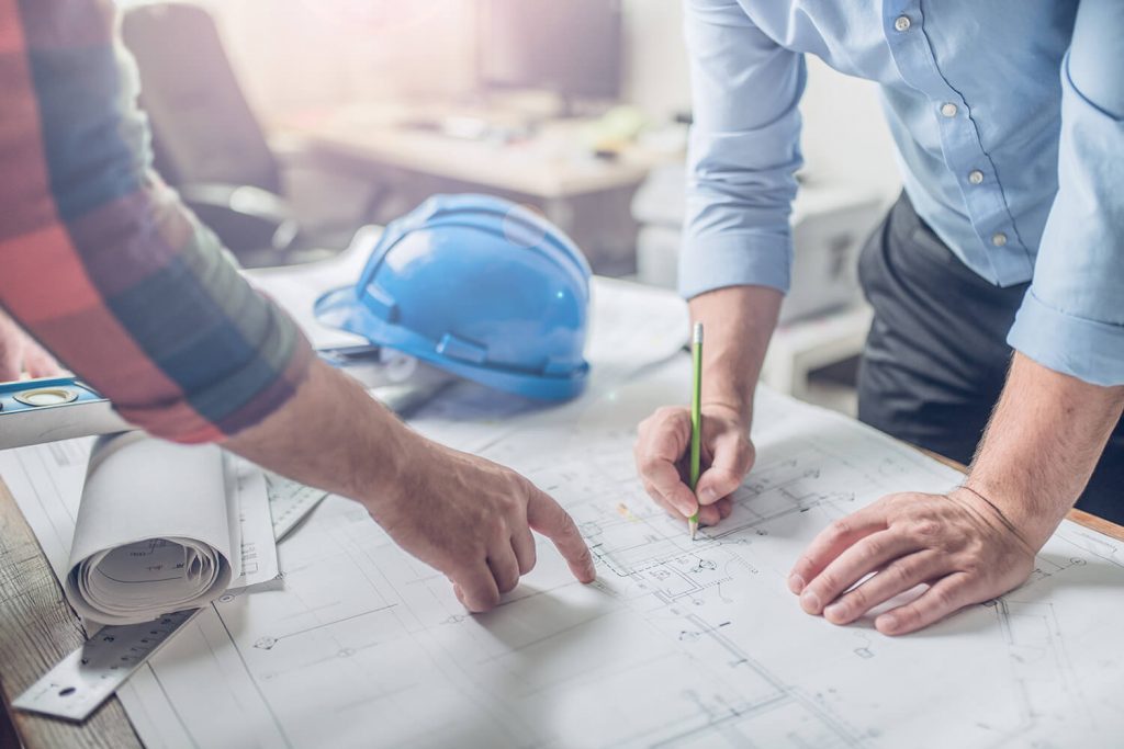 An architect and an engineer point at house plans laid out on a table