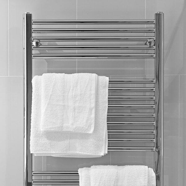 chrome towel rack mounted against a tiled wall with two sets of white cotton towels